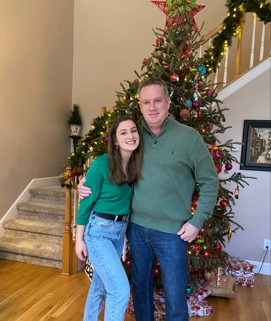 Rachel and her dad stand in front of a decorated Christmas tree.